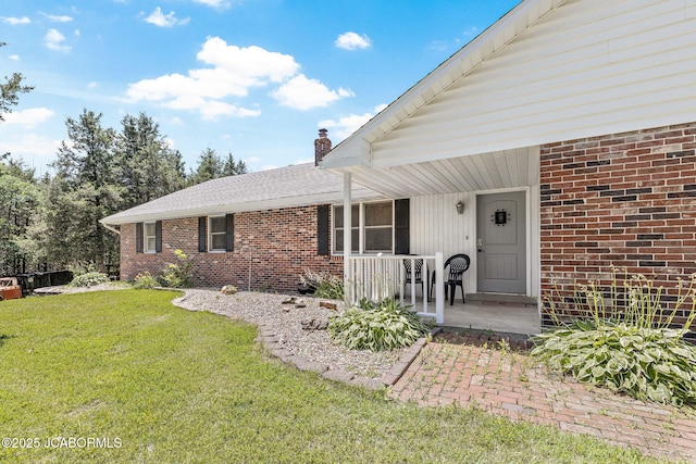 entrance to property featuring a yard, brick siding, a porch, and a chimney