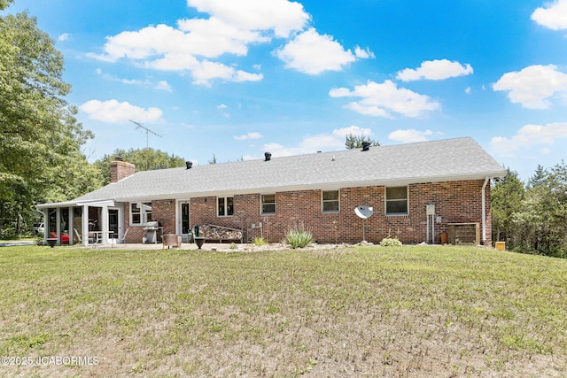 rear view of property featuring a lawn, a patio, a shingled roof, brick siding, and a chimney