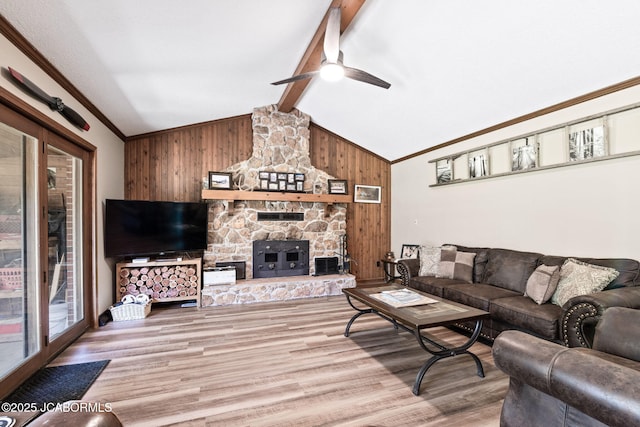 living room featuring vaulted ceiling with beams, wood walls, ornamental molding, a stone fireplace, and light wood-style floors