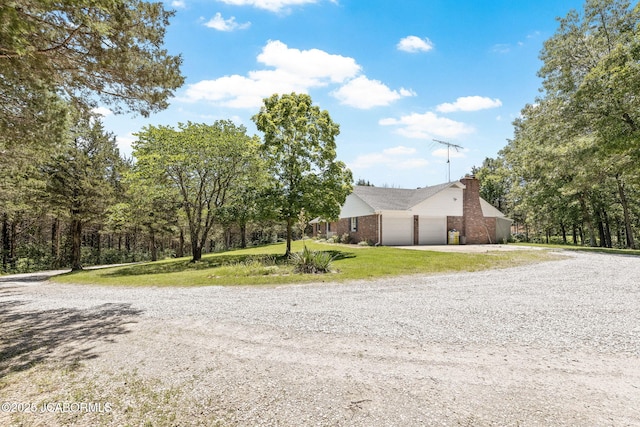 view of front facade with a front yard, gravel driveway, a chimney, a garage, and brick siding