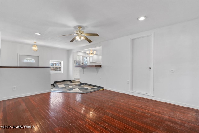 unfurnished living room featuring recessed lighting, baseboards, wood-type flooring, and ceiling fan with notable chandelier