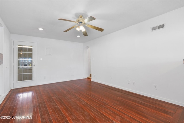 unfurnished room with visible vents, a ceiling fan, hardwood / wood-style floors, arched walkways, and baseboards