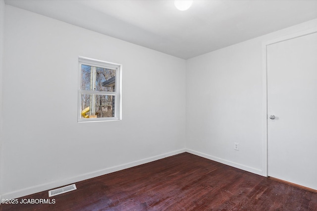 spare room featuring visible vents, baseboards, and dark wood-style floors