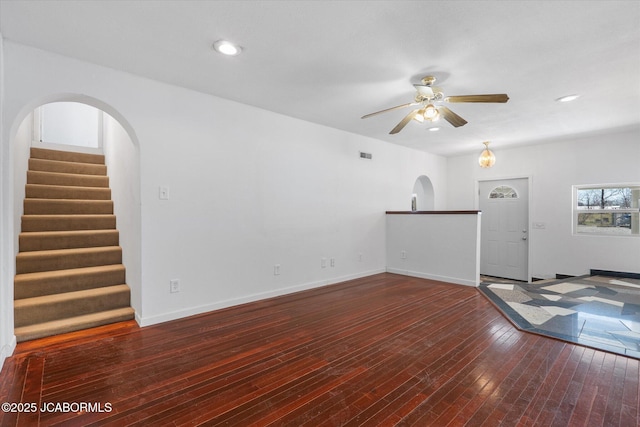 unfurnished living room featuring visible vents, ceiling fan, stairway, arched walkways, and wood-type flooring