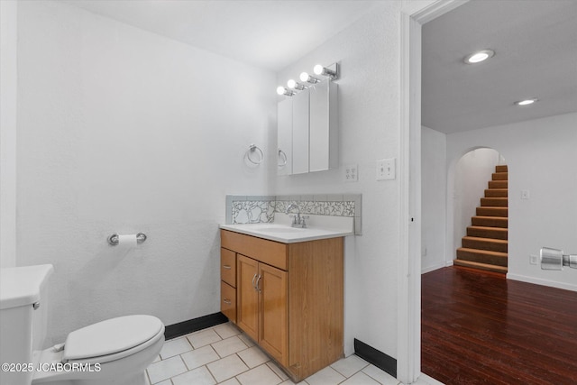 half bath featuring vanity, toilet, wood finished floors, and baseboards