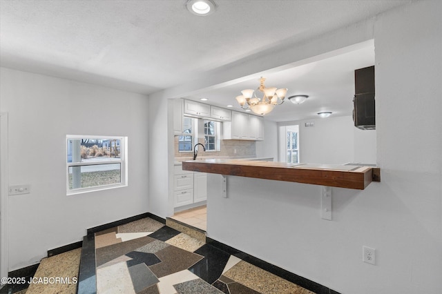 kitchen featuring a breakfast bar area, baseboards, an inviting chandelier, decorative backsplash, and white cabinetry