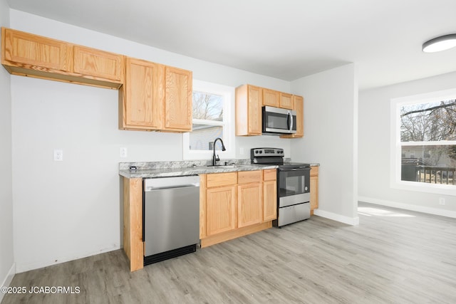 kitchen with light wood finished floors, stainless steel appliances, a sink, and light brown cabinetry