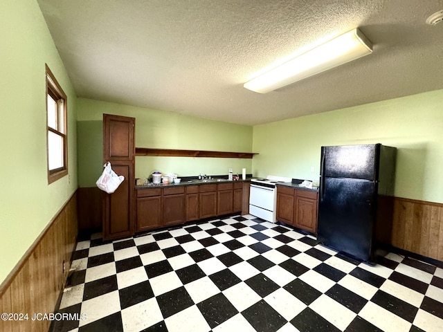 kitchen with black fridge, a textured ceiling, white range with electric stovetop, and wood walls