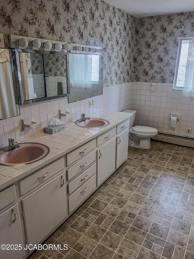 full bath featuring toilet, wallpapered walls, a sink, and a wainscoted wall