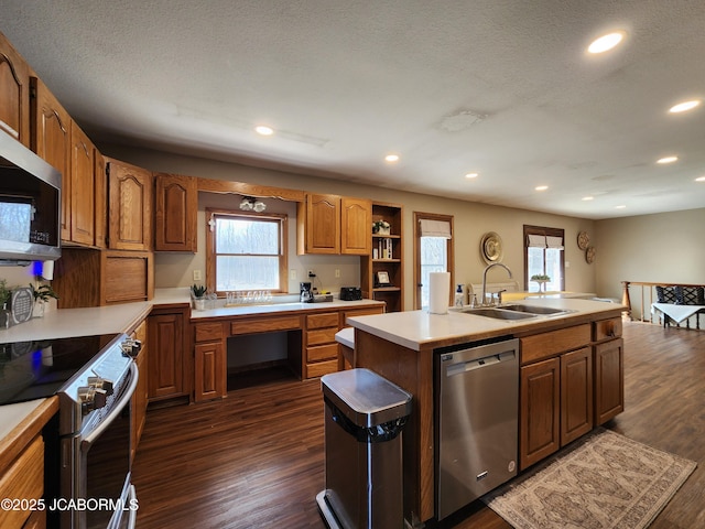 kitchen featuring a center island with sink, dark wood-style flooring, stainless steel appliances, light countertops, and a sink