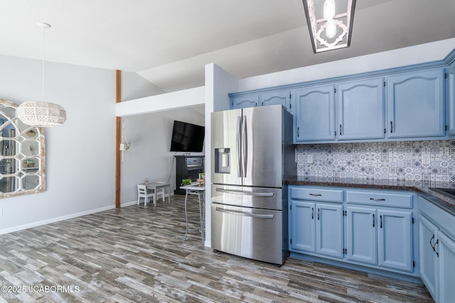 kitchen featuring blue cabinetry, tasteful backsplash, vaulted ceiling, wood finished floors, and stainless steel fridge