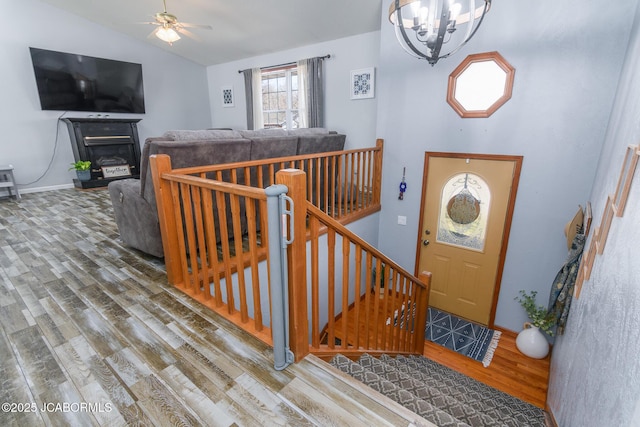 foyer with lofted ceiling, ceiling fan with notable chandelier, wood finished floors, baseboards, and a glass covered fireplace