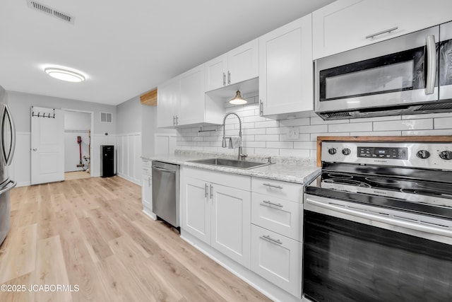 53036 Bird Haven Rd, Centertown, MO 65023 - kitchen featuring appliances with stainless steel finishes, white cabinets, light wood-style floors, and decorative backsplash