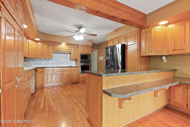 907 Primrose Ln, Jefferson City, MO 65109 - kitchen with appliances with stainless steel finishes, a peninsula, light wood-style floors, a kitchen breakfast bar, and decorative backsplash