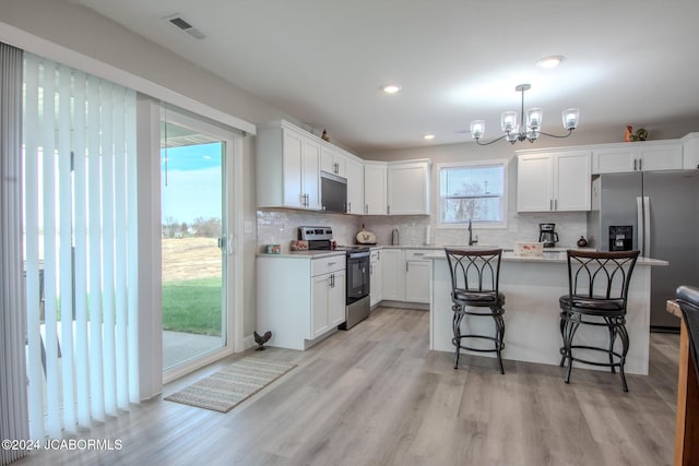 kitchen featuring appliances with stainless steel finishes, light wood-type flooring, a breakfast bar, pendant lighting, and white cabinets