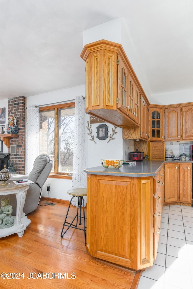 kitchen with kitchen peninsula, decorative backsplash, light wood-type flooring, and a breakfast bar area