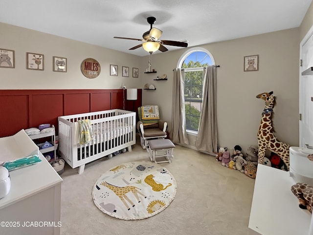 604 Mustang Dr, Ashland, MO 65010 - bedroom with a crib, light colored carpet, a ceiling fan, wainscoting, and a decorative wall