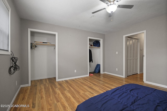 bedroom featuring a ceiling fan, a textured ceiling, wood finished floors, baseboards, and two closets