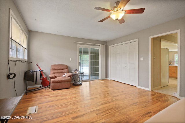 sitting room with light wood-style floors, a ceiling fan, and baseboards