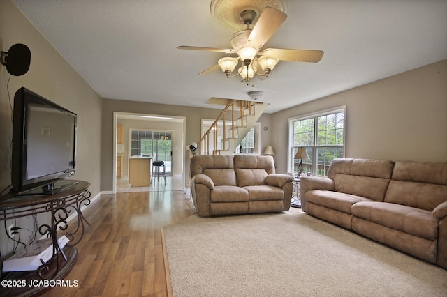 living area featuring baseboards, ceiling fan, wood finished floors, and stairway
