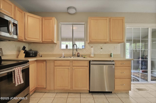 kitchen with appliances with stainless steel finishes, tasteful backsplash, a sink, light countertops, and light brown cabinets