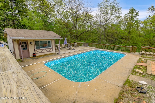 view of swimming pool featuring a deck, an outbuilding, an exterior structure, a fenced in pool, and a patio