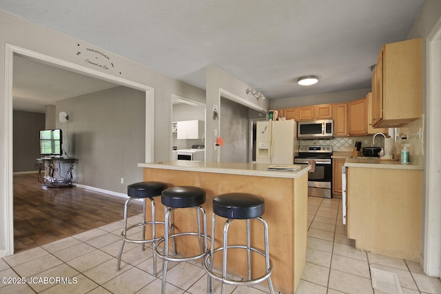 kitchen with appliances with stainless steel finishes, a breakfast bar, light countertops, washer / clothes dryer, and light tile patterned floors