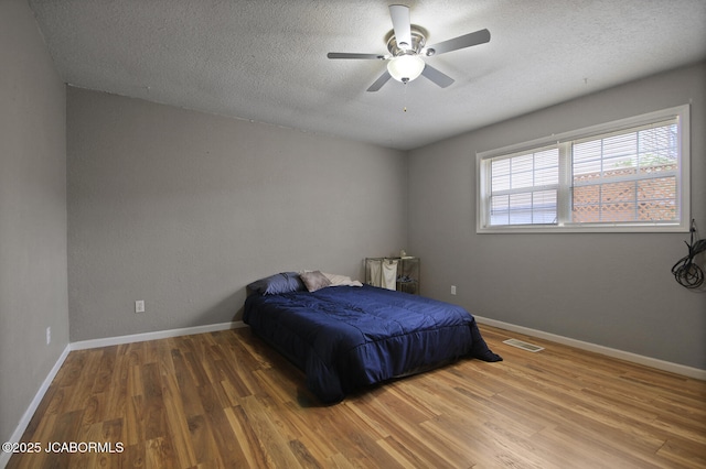 bedroom featuring ceiling fan, a textured ceiling, baseboards, wood finished floors, and visible vents