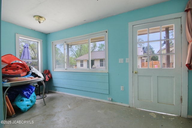 doorway to outside featuring baseboards and unfinished concrete flooring