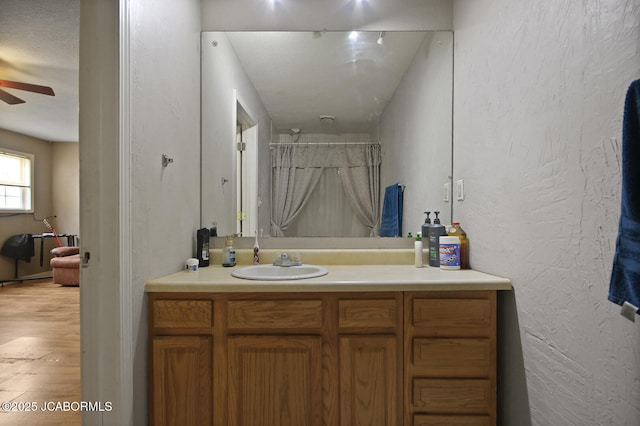 bathroom with vanity, a textured wall, wood finished floors, ceiling fan, and a shower with curtain