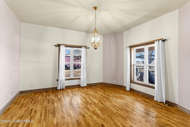 spare room with a healthy amount of sunlight, light wood finished floors, and a notable chandelier