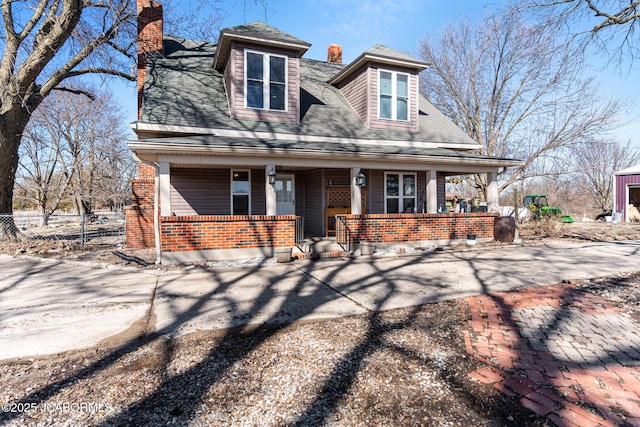 view of front of home with brick siding, a chimney, a shingled roof, covered porch, and fence