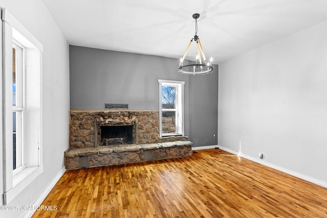 unfurnished living room featuring an inviting chandelier, baseboards, wood finished floors, and a stone fireplace