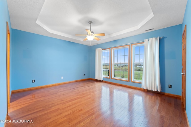 unfurnished room with ceiling fan, light hardwood / wood-style floors, a raised ceiling, and a textured ceiling