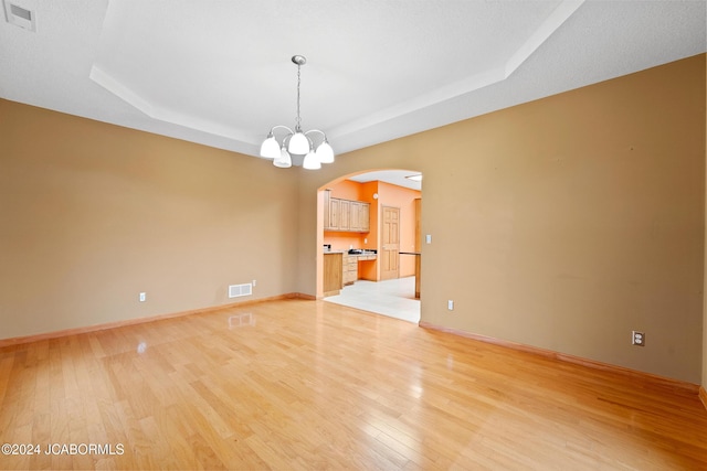 unfurnished room featuring a tray ceiling, light hardwood / wood-style flooring, and a notable chandelier