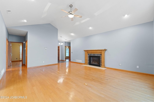 unfurnished living room with ceiling fan with notable chandelier, light hardwood / wood-style flooring, vaulted ceiling, and a tiled fireplace