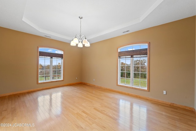 empty room featuring light wood-type flooring, a tray ceiling, an inviting chandelier, and plenty of natural light