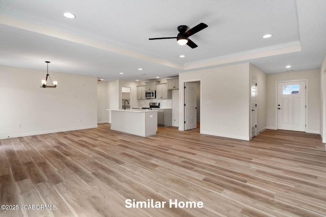 unfurnished living room with light wood finished floors, recessed lighting, a raised ceiling, and ceiling fan with notable chandelier