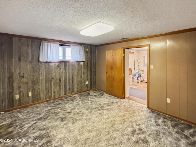 carpeted spare room with a textured ceiling and wood walls