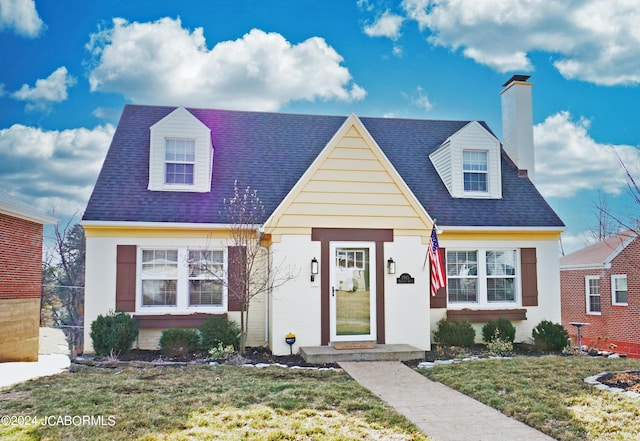 cape cod house with a chimney, roof with shingles, and a front yard