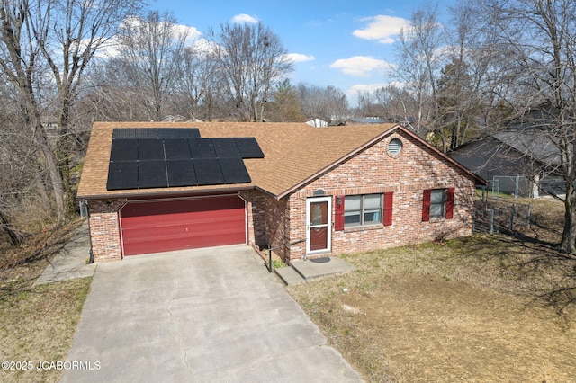 view of front facade with driveway, roof mounted solar panels, a shingled roof, a garage, and brick siding