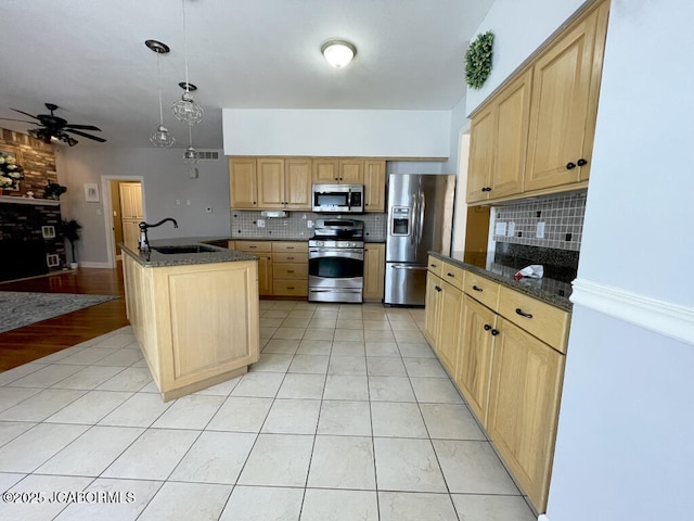 kitchen with sink, hanging light fixtures, light tile patterned floors, appliances with stainless steel finishes, and an island with sink