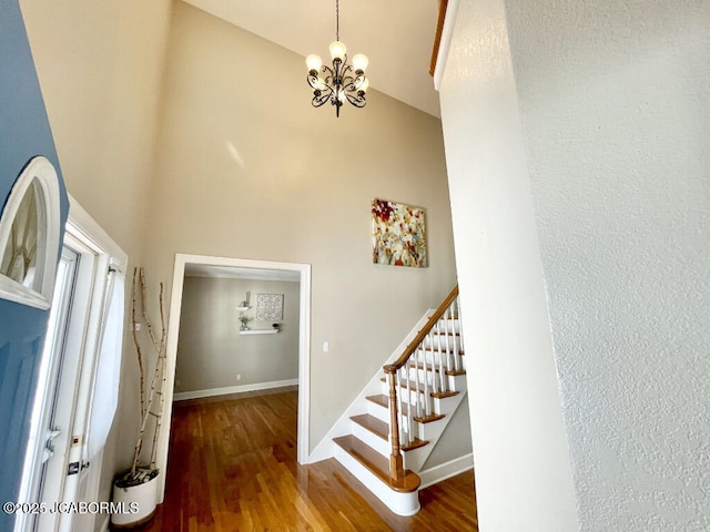 stairs with a towering ceiling, hardwood / wood-style floors, and a notable chandelier