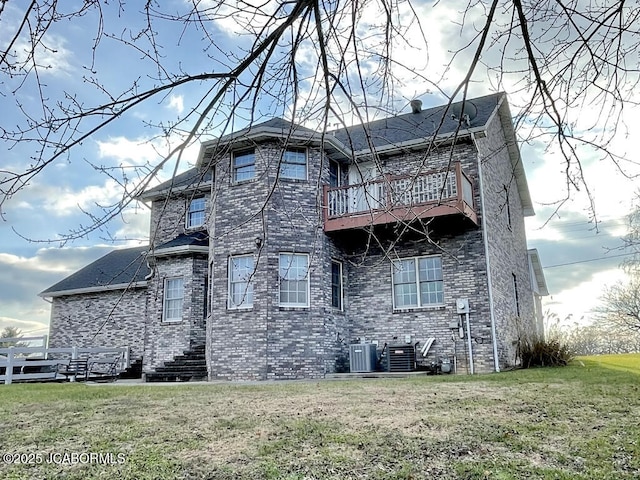 rear view of house with a balcony, a yard, and central AC