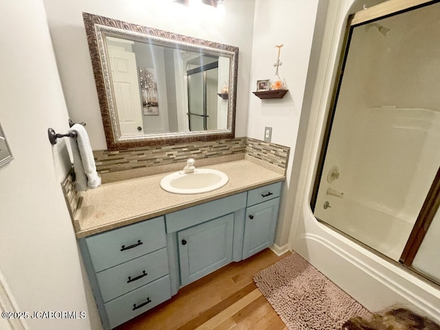 bathroom with vanity, combined bath / shower with glass door, hardwood / wood-style floors, and backsplash