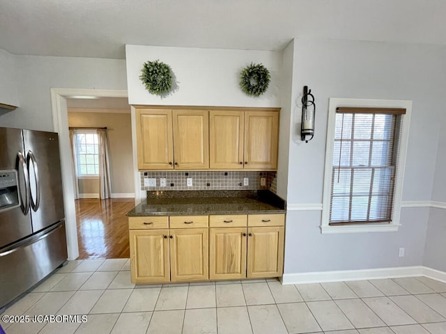 kitchen featuring stainless steel fridge with ice dispenser, backsplash, light tile patterned floors, and dark stone counters