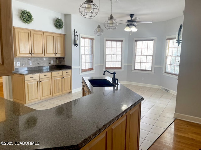 kitchen with decorative light fixtures, sink, dark stone countertops, decorative backsplash, and a center island with sink