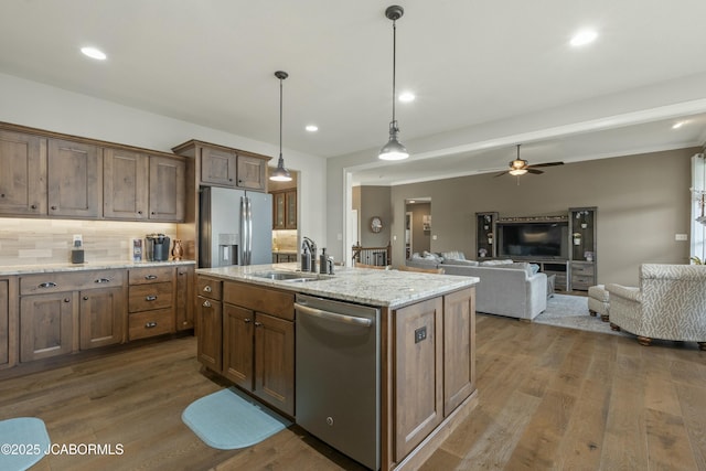 kitchen with an island with sink, appliances with stainless steel finishes, ceiling fan, a sink, and dark wood-style floors