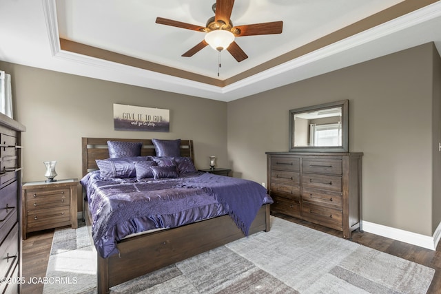 bedroom with wood finished floors, a ceiling fan, a tray ceiling, and baseboards