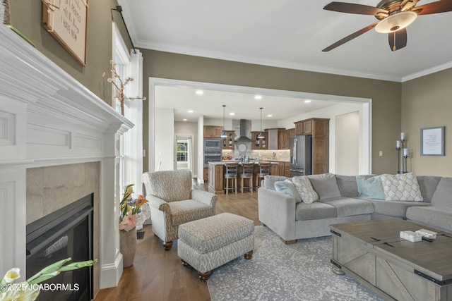 living room with ornamental molding, a tile fireplace, a ceiling fan, and wood finished floors
